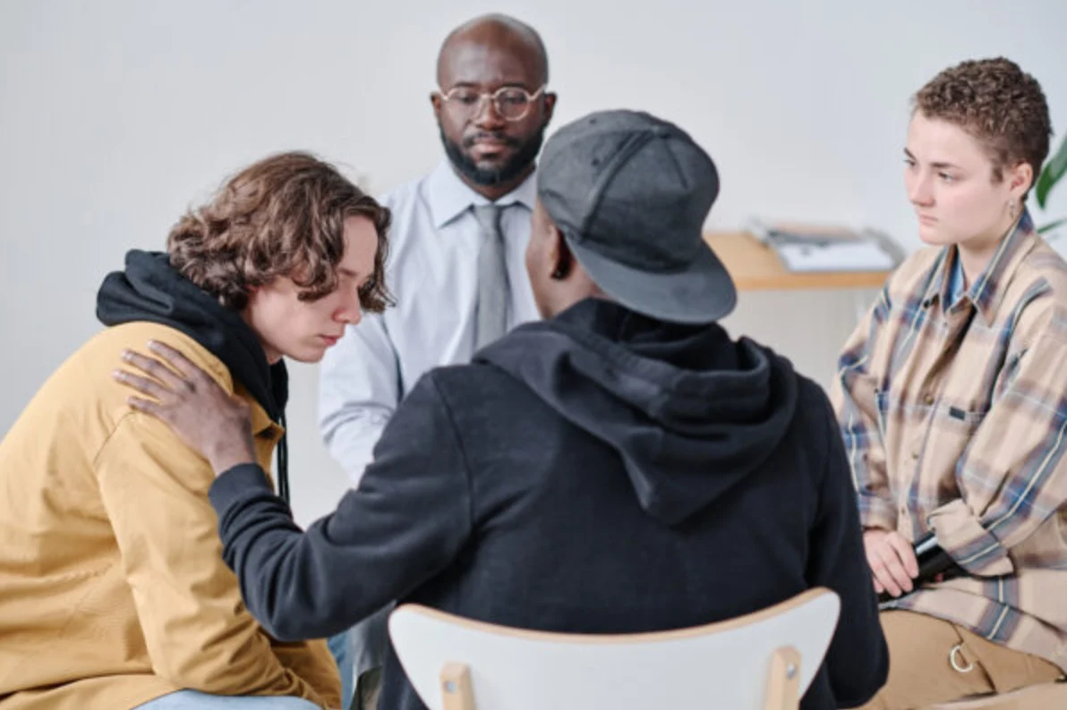 Teenage boy talking about problems to other people while they supporting him and giving advice during psychotherapy session